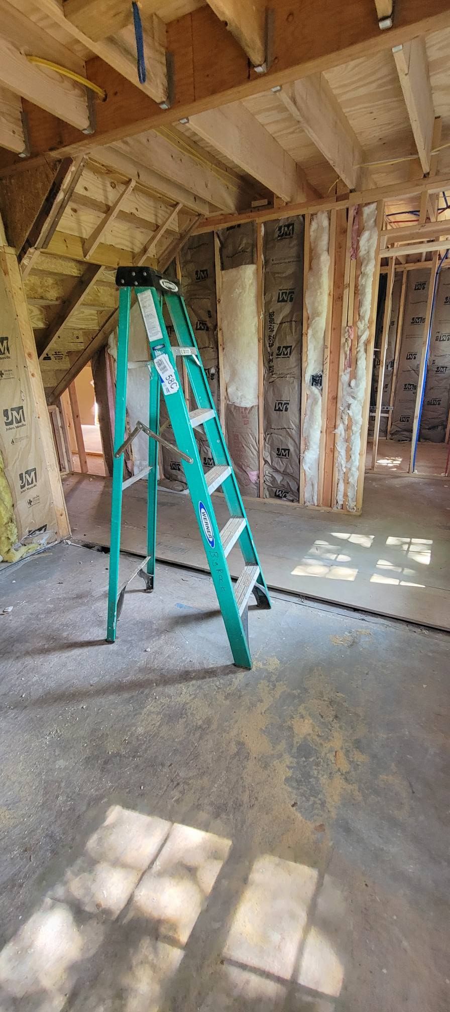 A green ladder in a room under construction, with exposed wooden beams and framing.