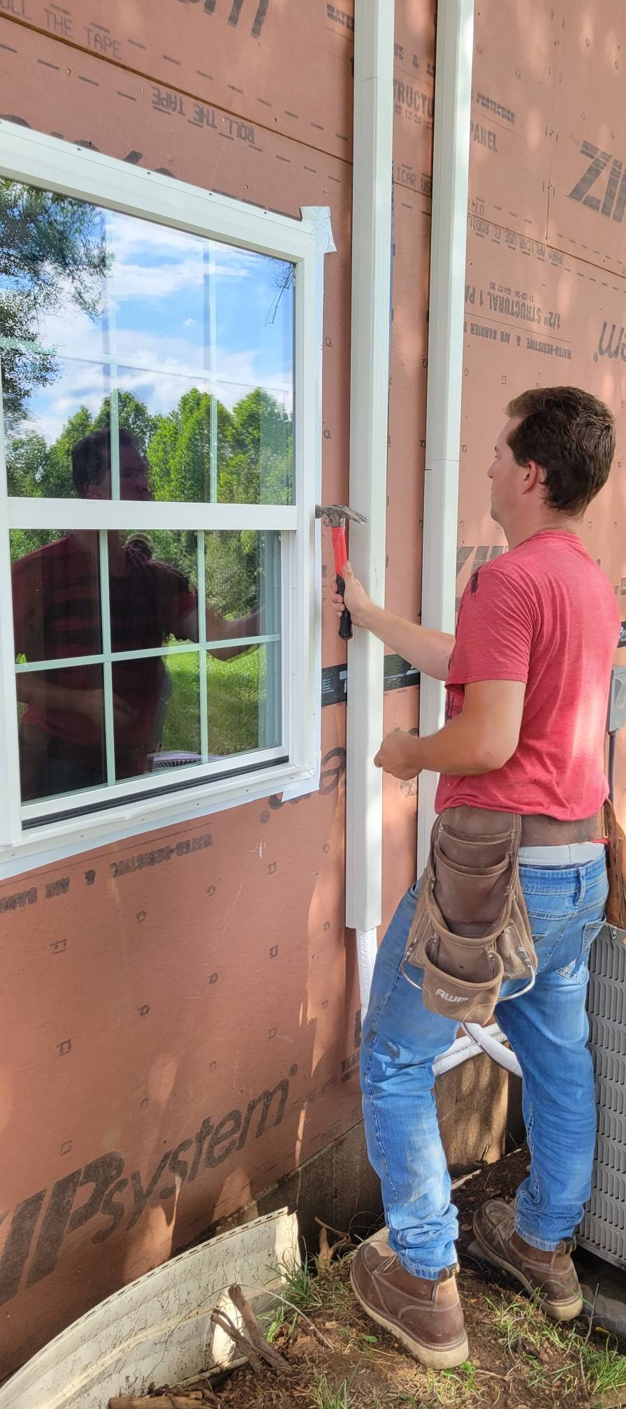 A person uses a hammer on white trim near a window of a building.