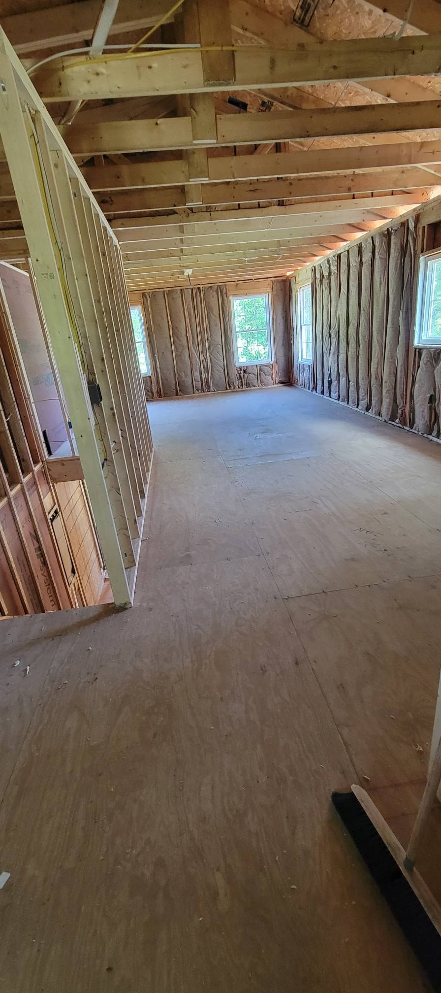 Interior view of a building under construction, featuring exposed wooden beams and framing with a bare plywood floor.