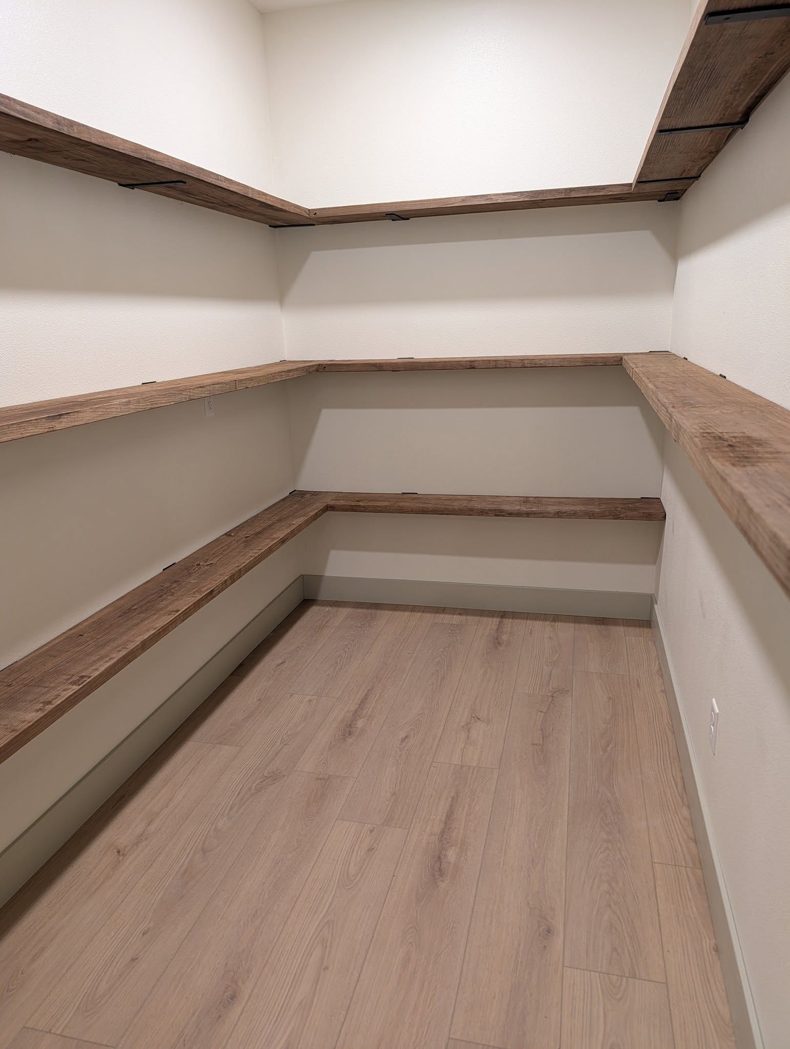 Empty pantry with wooden shelves against white walls, light wood flooring.