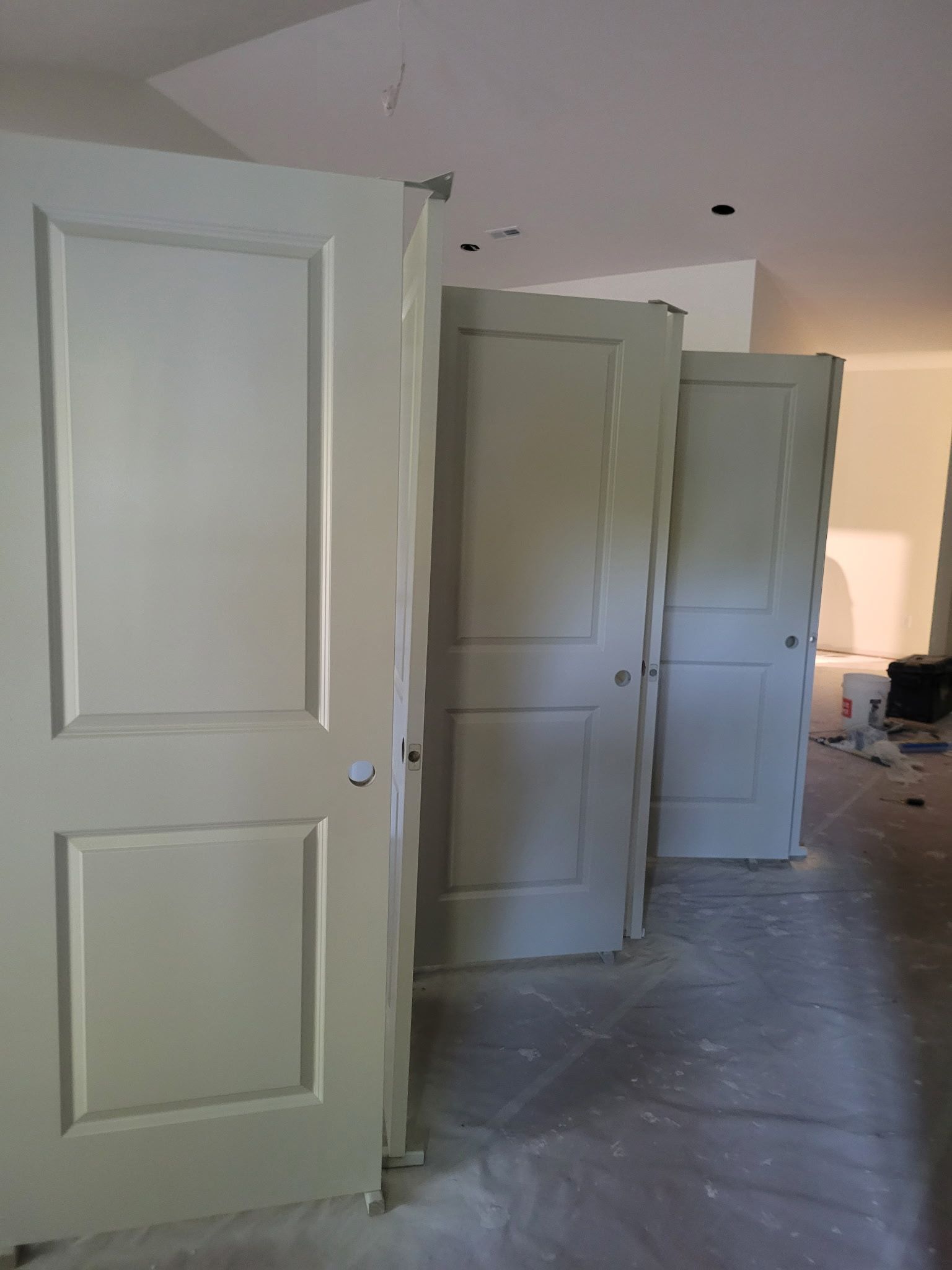 Three white, two-panel interior doors propped up in a room with a light gray floor, possibly under construction.