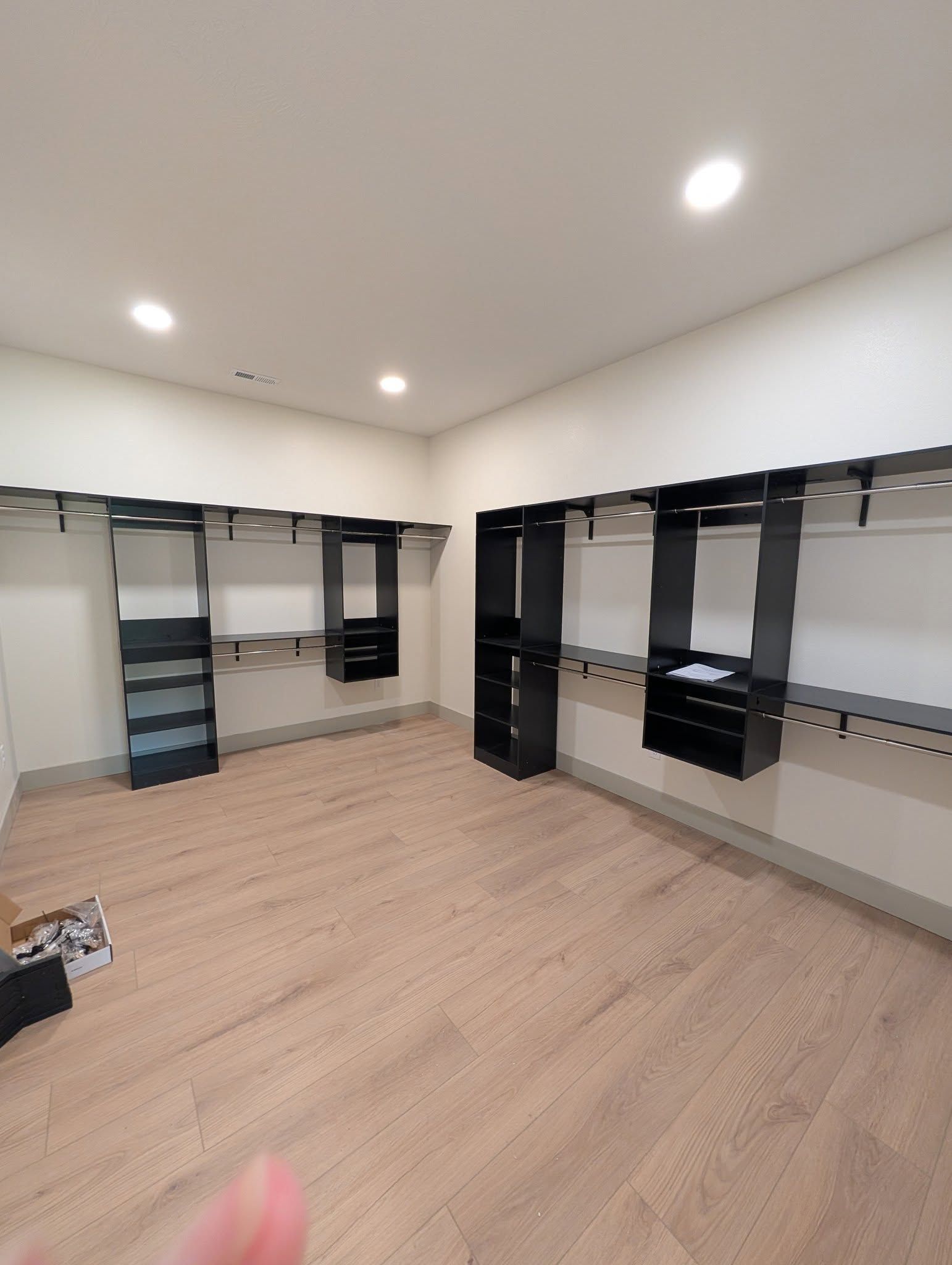Empty walk-in closet with black shelving and hanging rods. Light wood floors and beige walls.