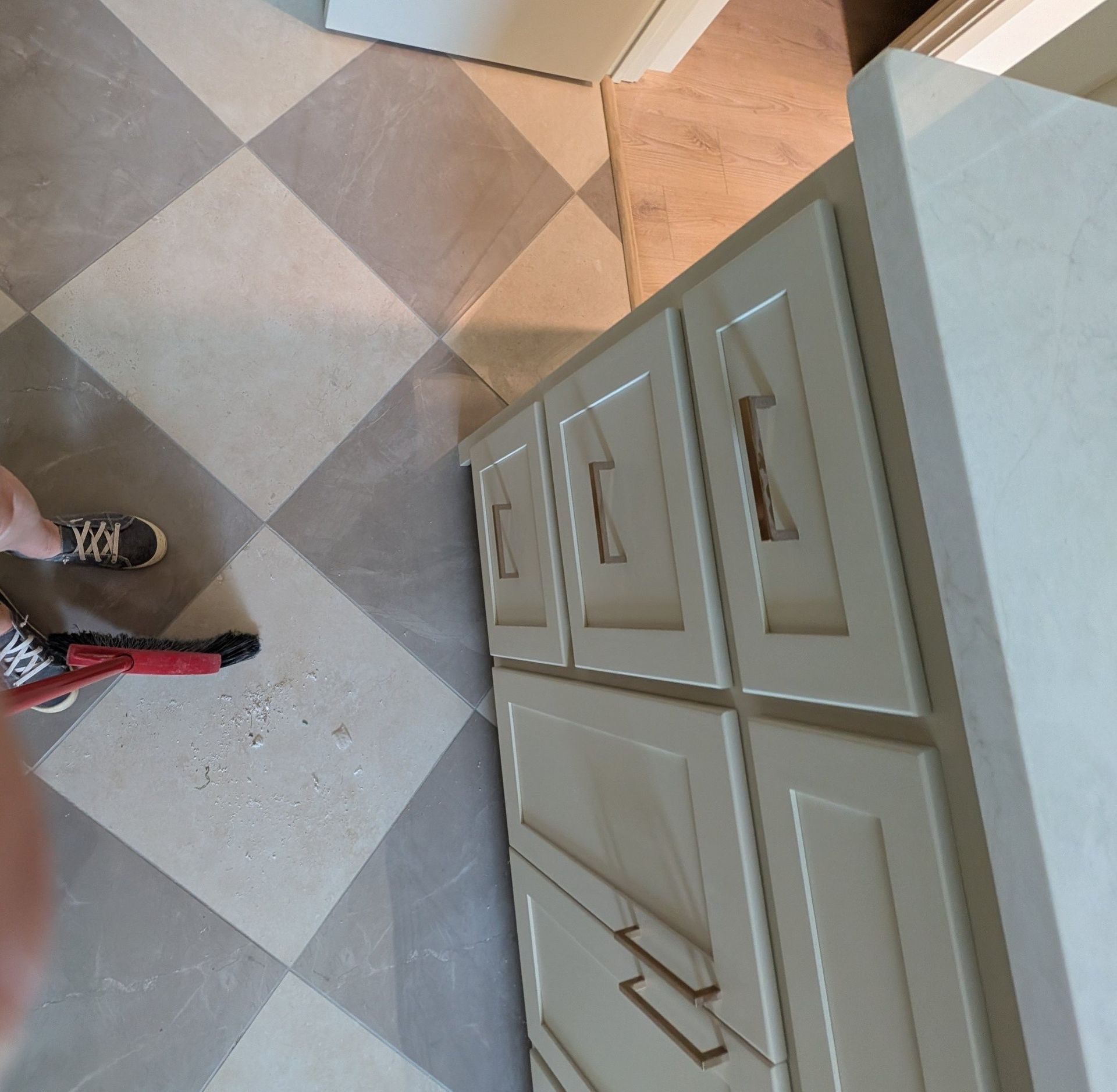 Light-colored bathroom cabinets with bronze handles against a tiled floor.