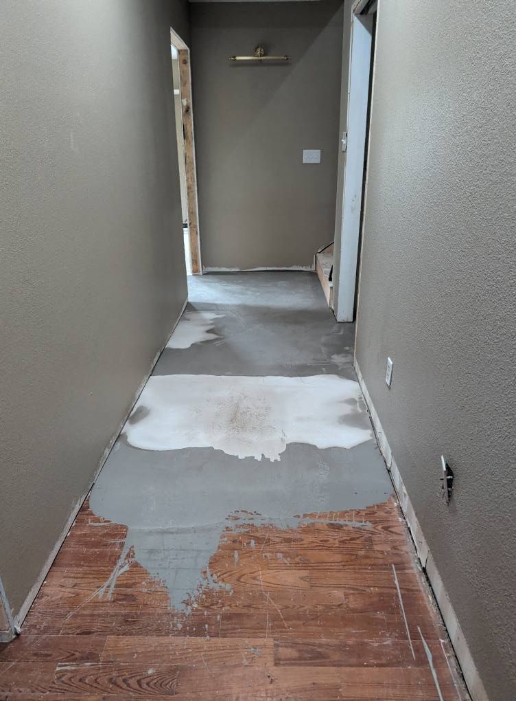 Hallway with wood-look flooring and concrete patch, leading to doorways. Brown walls.