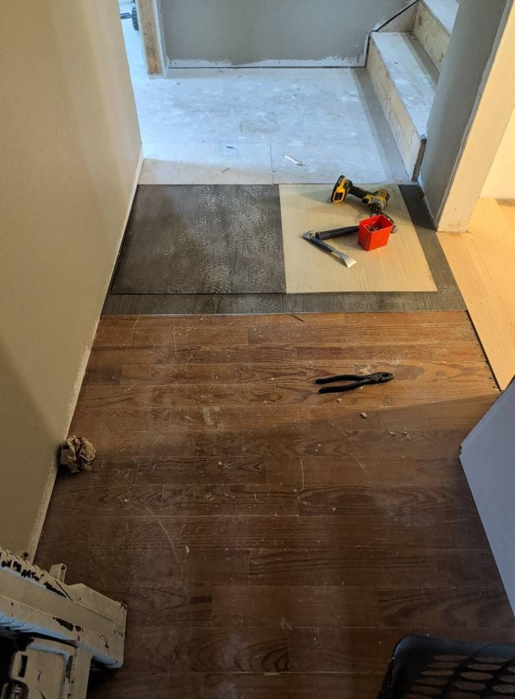 Wooden flooring installation in progress; tools and carpet on the floor near a stairway.