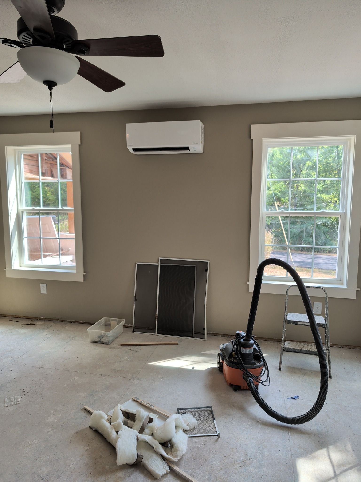 Room under construction with a mini-split AC unit, two windows, and a vacuum cleaner.