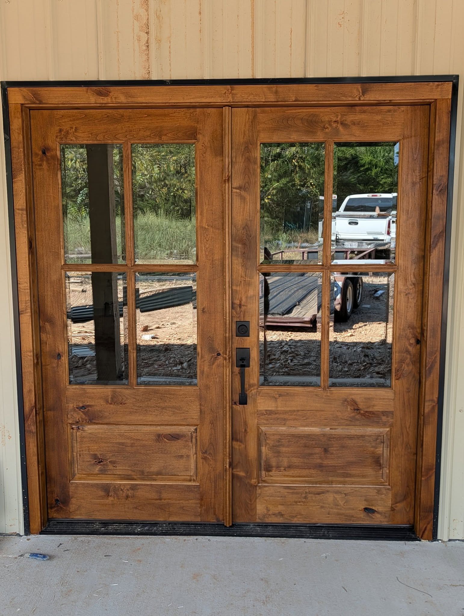 Double wooden doors with glass panes reflecting a truck and trailer, stained medium brown.