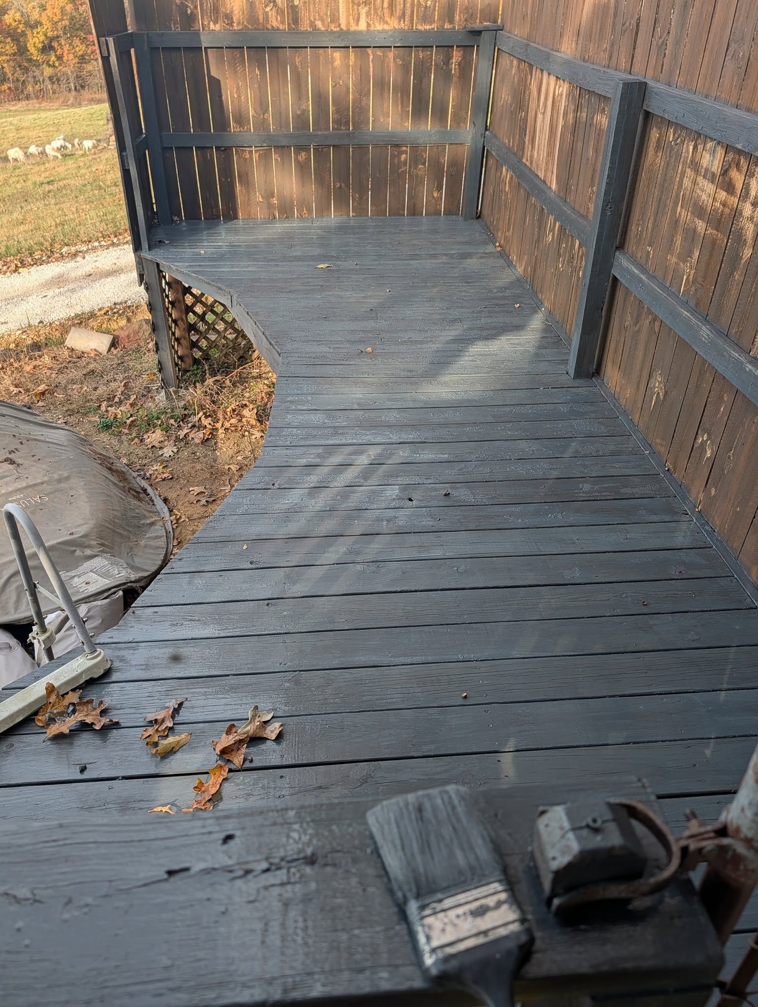 Wooden deck painted dark gray, with a matching railing and tools on the deck.