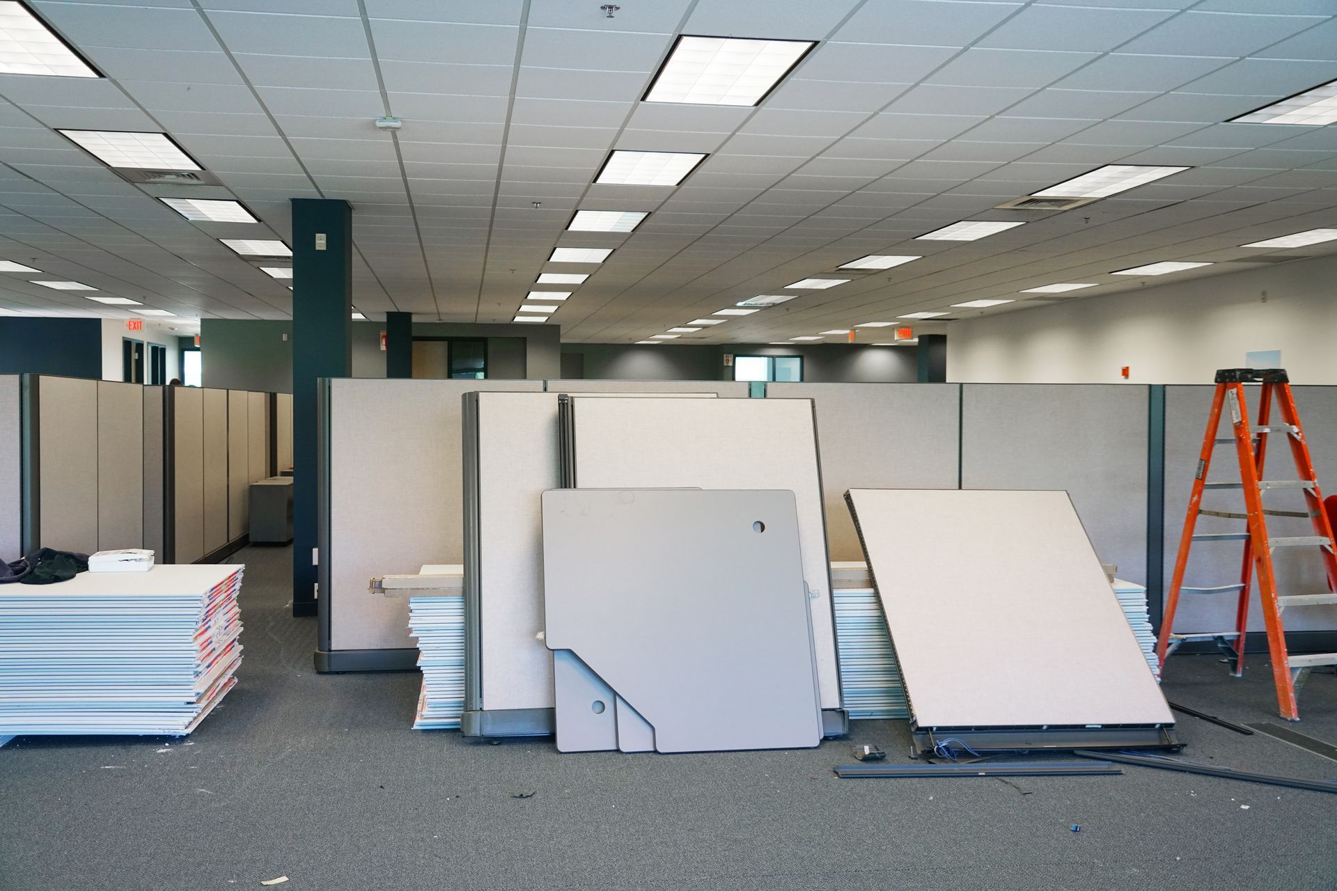 Empty office space during renovation, cubicle walls and panels piled on floor, orange ladder.— Walnut Grove, MO — Big Rock Construction Empty office space during renovation, cubicle walls and panels piled on the floor, orange ladder.