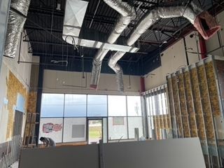 Interior of a building under construction, showing ductwork, exposed framing, and large windows.