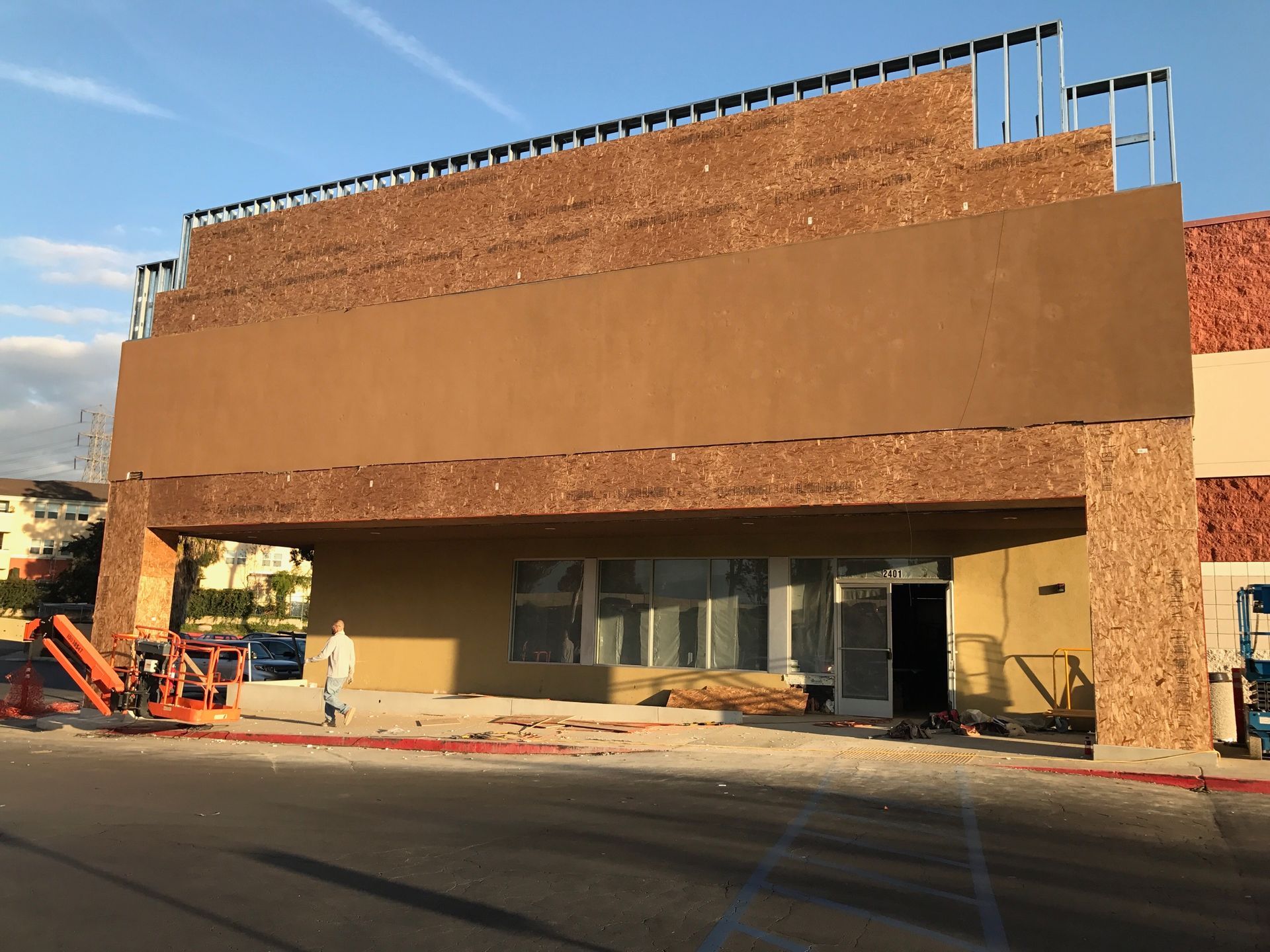 Building under construction with brown facade and open doorway; worker near lift.