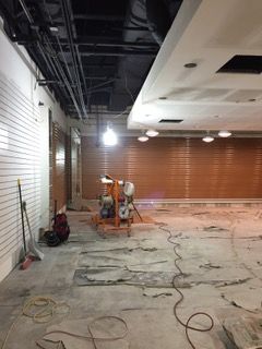Interior construction site with exposed wiring, concrete floor, and orange security shutters.