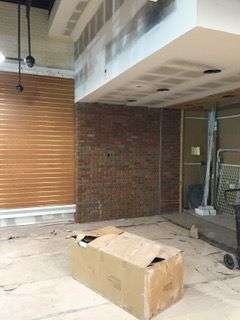 Interior view of a construction site with exposed brick wall, cardboard box, and a closed metal shutter.