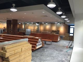 Interior of a space under construction, with tiered wooden structures, exposed materials, and overhead lighting.