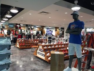 Interior of a sports apparel store with shoe displays, clothing racks, and a mannequin wearing a blue shirt.