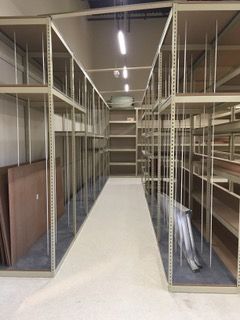 Empty beige shelving unit in a narrow storage hallway, with dividers and a ladder.