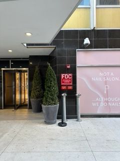 Entrance to a building with two potted trees, security camera, and a sign for a nail salon.