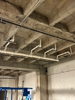 Concrete ceiling with pipes and wiring. White pipes are connected to the ceiling, with a black pipe above them.