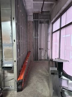 Construction site with metal framing, ladder, unfinished walls, and a window with pink tint.