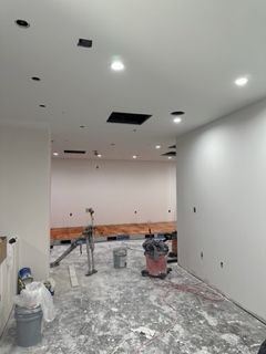 Interior of a room under construction with white walls, recessed lighting, and exposed floor.