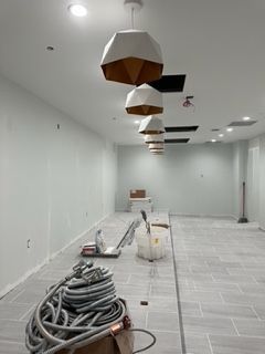 Interior construction site with gray tile floor, white walls, and geometric pendant lights.