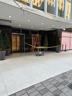 Building entrance with caution tape, ladder, and construction materials.