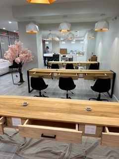 Salon with wooden tables, black chairs, and overhead lights; a cherry blossom tree sits in the corner.