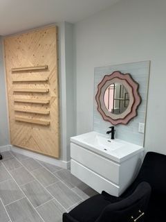 Modern bathroom: white floating vanity with black faucet, unique mirror, wood accent wall, black chair.