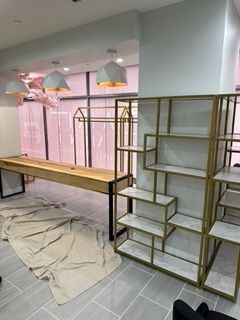Interior of a clothing store with shelving, display racks, and a wooden table.