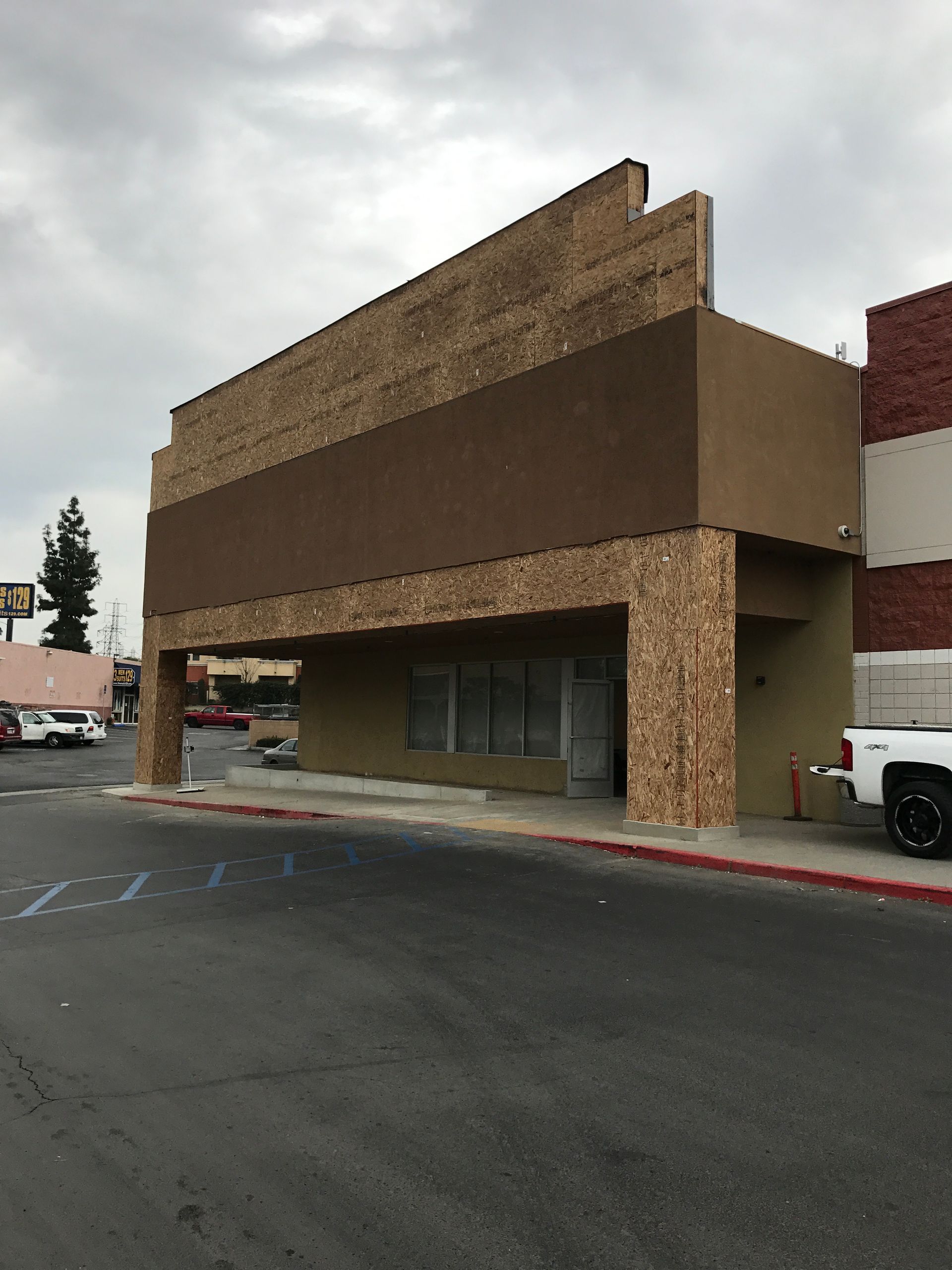Exterior of a commercial building with brown brick facade and support pillars. Paved parking area.
