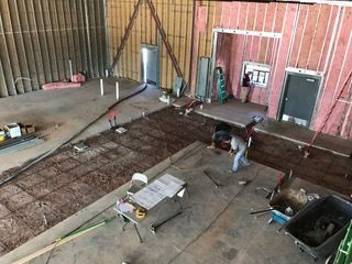 Construction site: workers pouring concrete. Interior with framing, rebar, and tools.