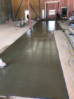 Freshly poured concrete floor in a commercial space under construction. Construction workers are visible in the background.