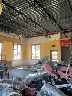 Interior renovation: metal ceiling beams, yellow walls, windows, debris and HVAC ducts on the floor.