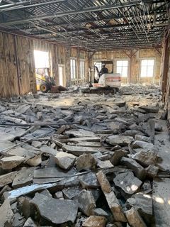 Interior demolition of a building with rubble on the floor; construction equipment visible.