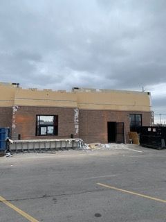 Building exterior under construction with exposed brick, open door, and cloudy sky.