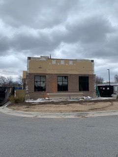 Building under construction with brick facade, three dark windows, and cloudy sky.