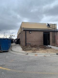 Building under construction with a brick exterior and a person on the roof. Dumpsters and a ladder are present.