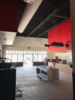 Interior of a commercial space under construction; open storefront, red accents, exposed ceiling, and a man in the background.