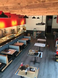 Restaurant interior under construction, red and gray walls, booths, tables, exposed beams, lighting fixtures.