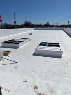 White commercial roof with two skylights and surrounding structures under a bright blue sky.