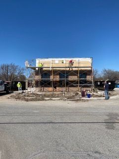 Building under construction with scaffolding and workers. Brick and stucco exterior. Sunny day.