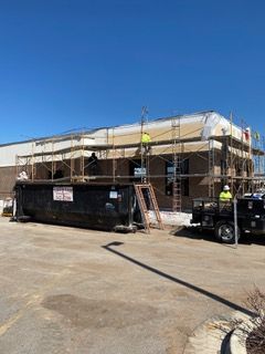 Building under construction with scaffolding and a dumpster; two workers visible.