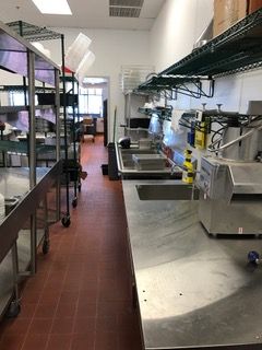 Stainless steel commercial kitchen with shelving, counter, and equipment. Red tile floor.