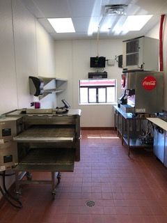 Commercial kitchen with stainless steel appliances, a pizza oven, and a Coca-Cola soda dispenser.