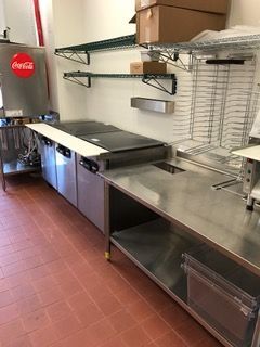 Commercial kitchen with stainless steel counters, cooking equipment, shelves, and a Coca-Cola dispenser.
