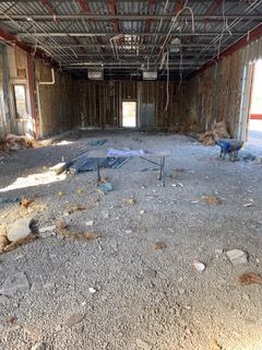Interior of a gutted building with exposed beams, rubble on the floor, and a small door at the end.