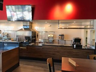 Restaurant interior with counter, kitchen equipment, red wall, and a television.