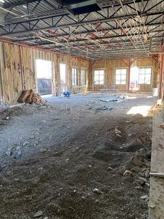 Interior of unfinished building with dirt floor, wooden walls, metal ceiling beams, and windows.