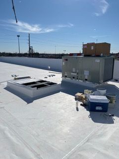 White commercial roof with HVAC units, skylight, and supplies under a bright blue sky.
