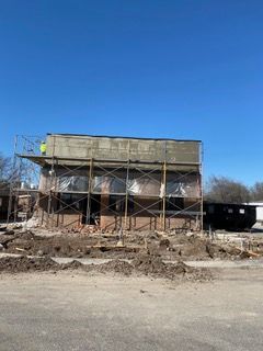 Building under construction with scaffolding; a worker is on top.